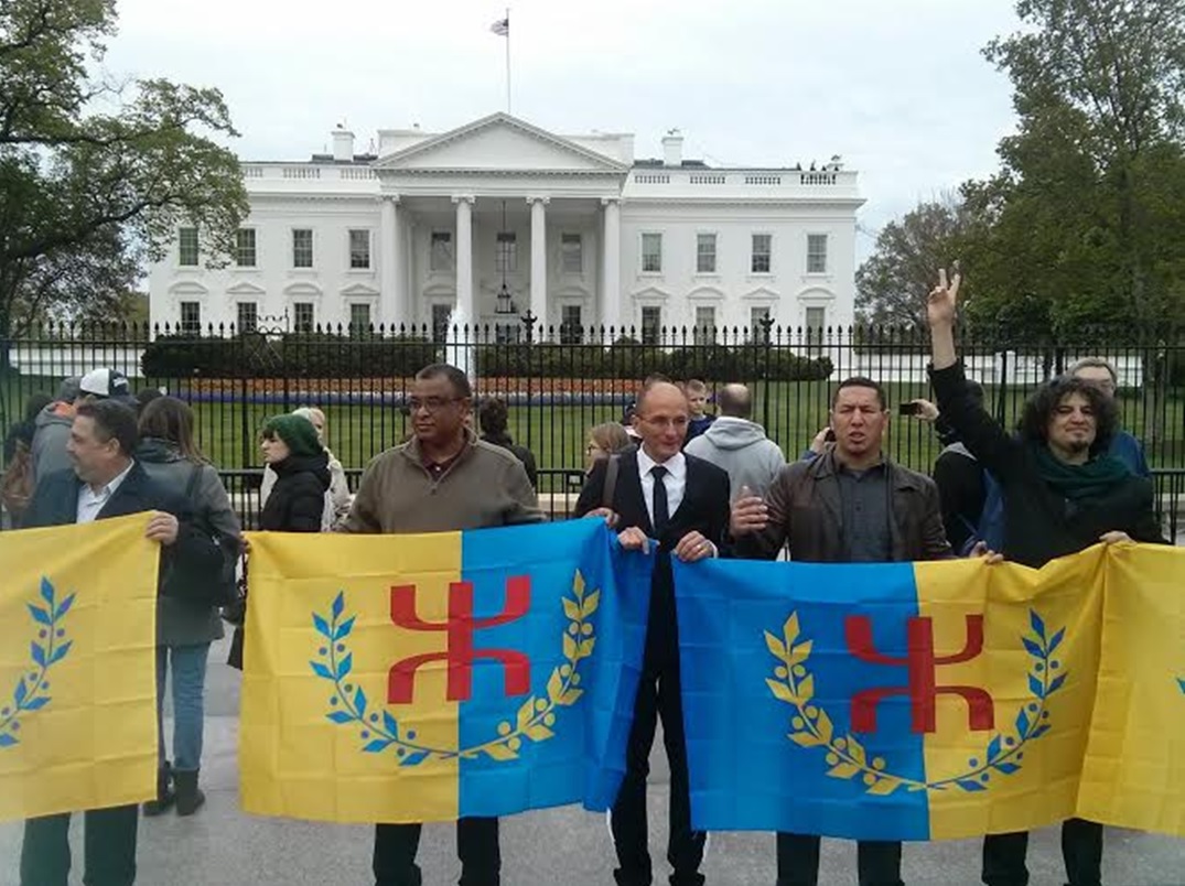 Karim Akouche devant la Maison Blanche à Washington brandissant le drapeau kabyle et le V de la victoire